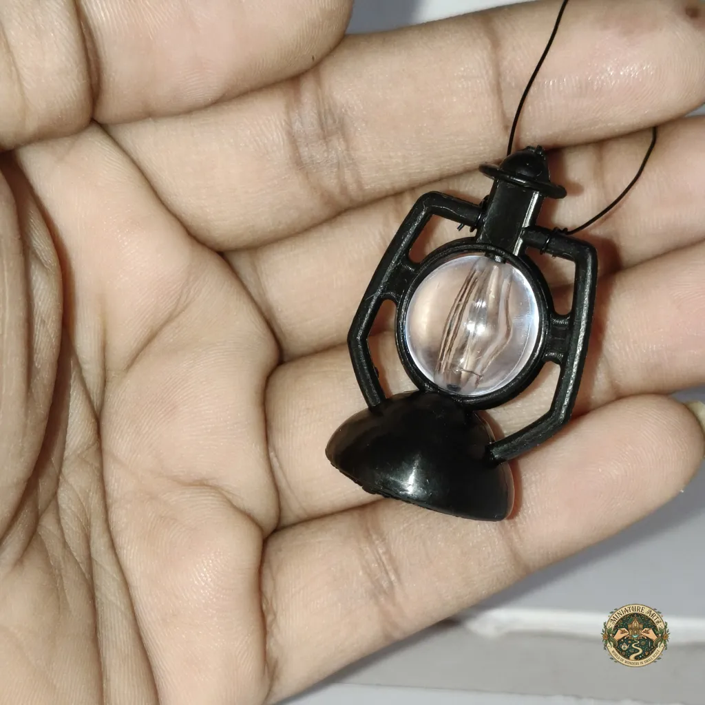 lantern-1 Close-up of the dollhouse lantern miniature product. The detailed item has a warm LED light glowing and is held between fingers for scale.