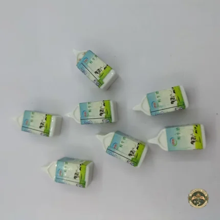 A hyper-realistic miniature milk packet product scaled for dollhouse kitchens, featuring detailed graphics and a sealed carton top.