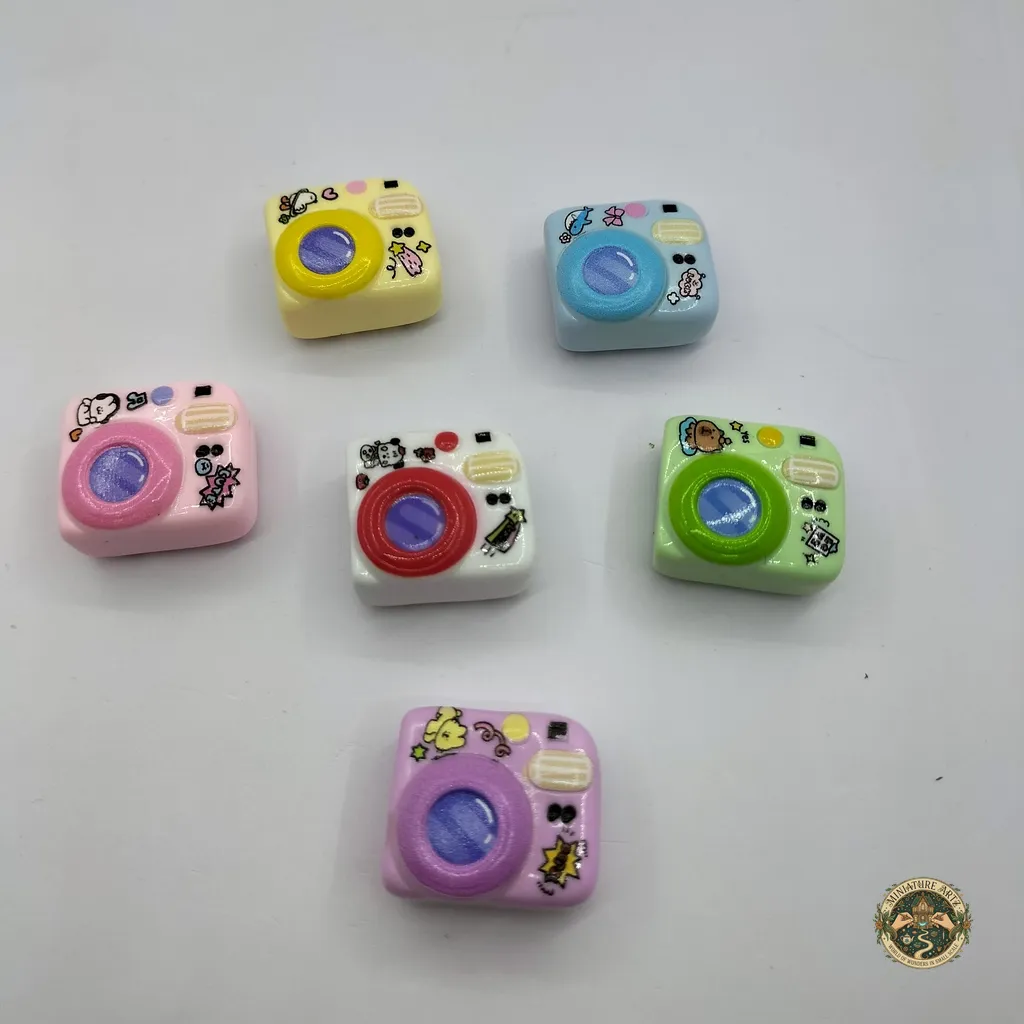 miniature-camera-1 A handcrafted vintage miniature camera product with intricate details, a black textured body, and a silver lens for dollhouse decor.