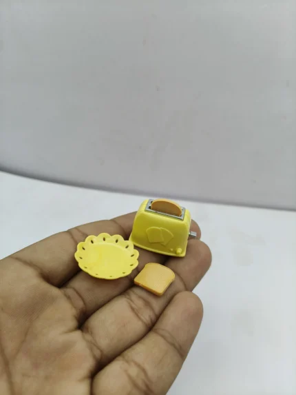 A miniature bread toaster product in a classic silver finish, shown with two tiny pieces of toast for a realistic dollhouse kitchen scene.