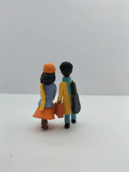 A detailed miniature winter couple product showing a man and woman in warm coats sitting closely together on a small park bench.