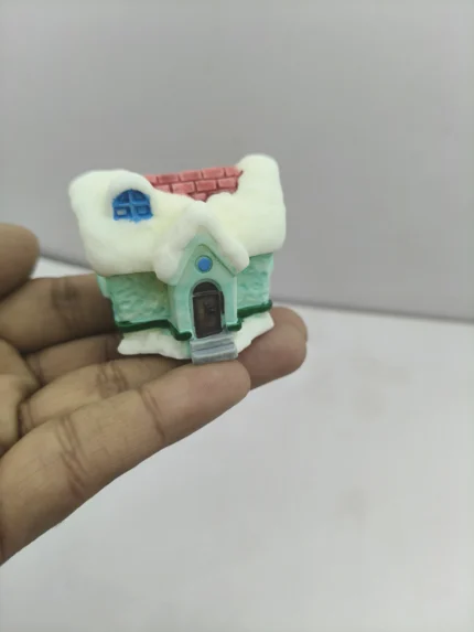 A charming green miniature winter home product with a snow-dusted roof and detailed windows, perfect for a holiday village display.