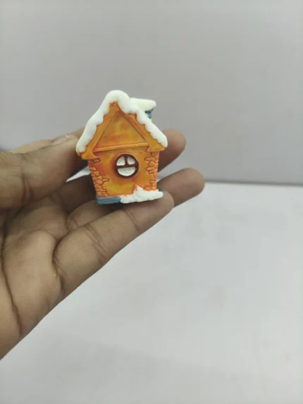 A vibrant orange miniature winter house product with a snow-dusted roof, detailed windows, and a charming chimney for holiday dioramas.