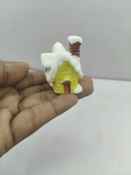 A charming miniature winter house product with a bright yellow exterior, a snow-dusted roof, and intricate window and door details.