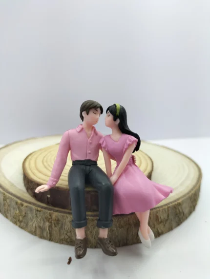 A couple miniature figurine product showing a man and woman sitting closely together on a bench in an affectionate, romantic pose.