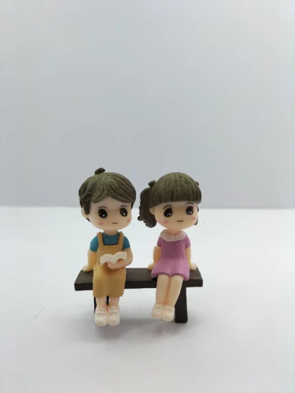 A detailed studying couple miniature product, showing a male and female figurine sitting at a small desk reading books together.