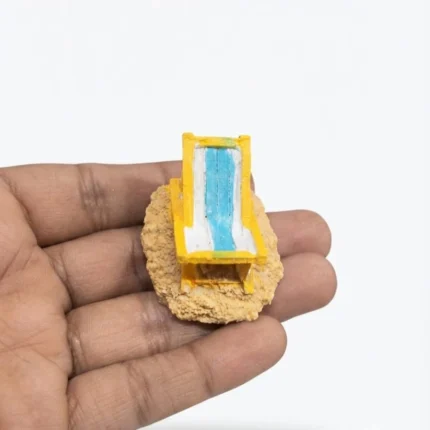 A detailed miniature beach lounge chair figurine on a sandy base, dollhouse or diorama product.