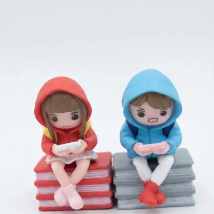 Chibi gamer couple figurine set of 2, a charming product sitting on miniature books, ideal for desk decor.