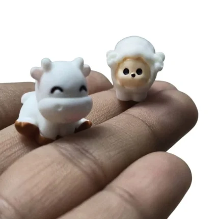 Product: Miniature cow and sheep figurine set. Detailed brown/white cow, white sheep on grassy base.