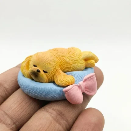 Charming miniature sleeping dog figurine product, resting peacefully on a blue cushion with a pink bow.