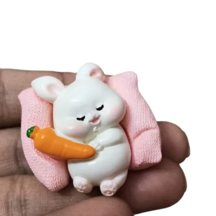 Miniature white rabbit figurine product holding a carrot, on a pink cushion base, for dollhouse scenes.