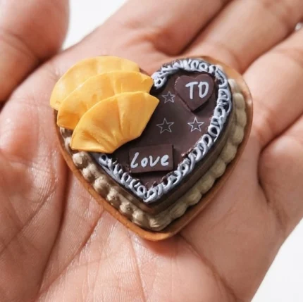 A charming miniature heart chocolate cake product, beautifully decorated with colorful fruit slices.