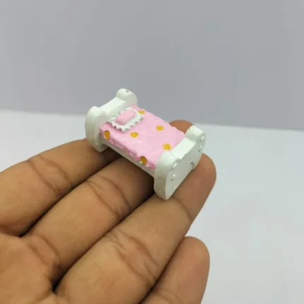 Miniature dollhouse bed with pink polka dot bedding. This product adds a cozy touch to any dollhouse bedroom.
