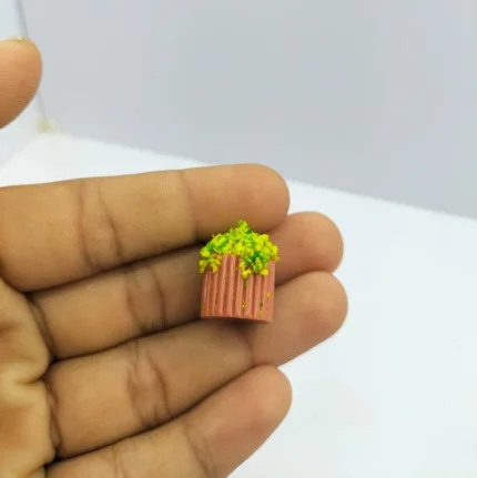 A detailed miniature green foliage plant in a pink ribbed square pot, a charming decorative product for dollhouses.