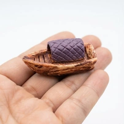 A detailed miniature sailing boat figurine product with a white woven sail, perfect for display or collection.