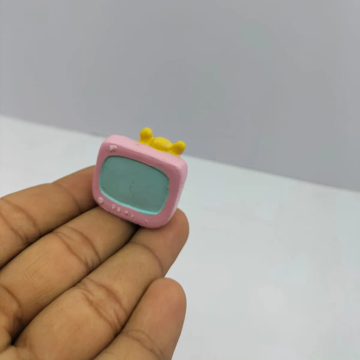 Pink-Miniature-Retro-Television-Figurine-1 A charming pink miniature retro television figurine, a delightful product for dollhouse enthusiasts and collectors.