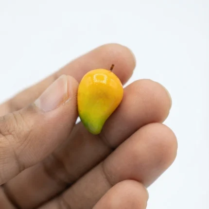 A detailed miniature yellow mango figurine product, perfect for dollhouse kitchens or fruit stand displays.