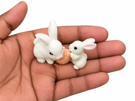 A charming miniature white rabbit pair holding a carrot, a delightful product for any dollhouse or diorama scene.